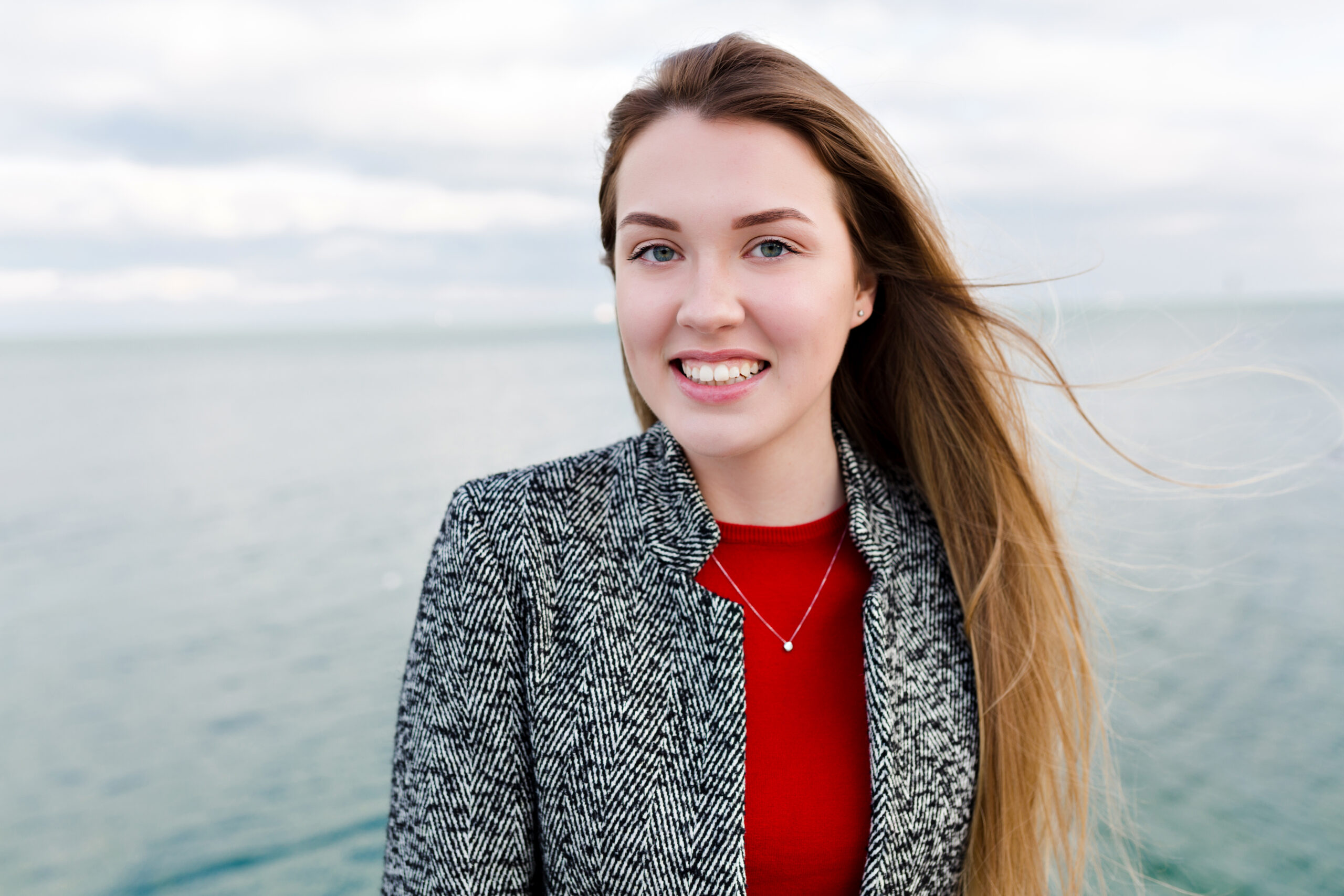 portrait of smiling pretty girl with flying long hair enjoys good weather and walking by the sea with true happy emotions