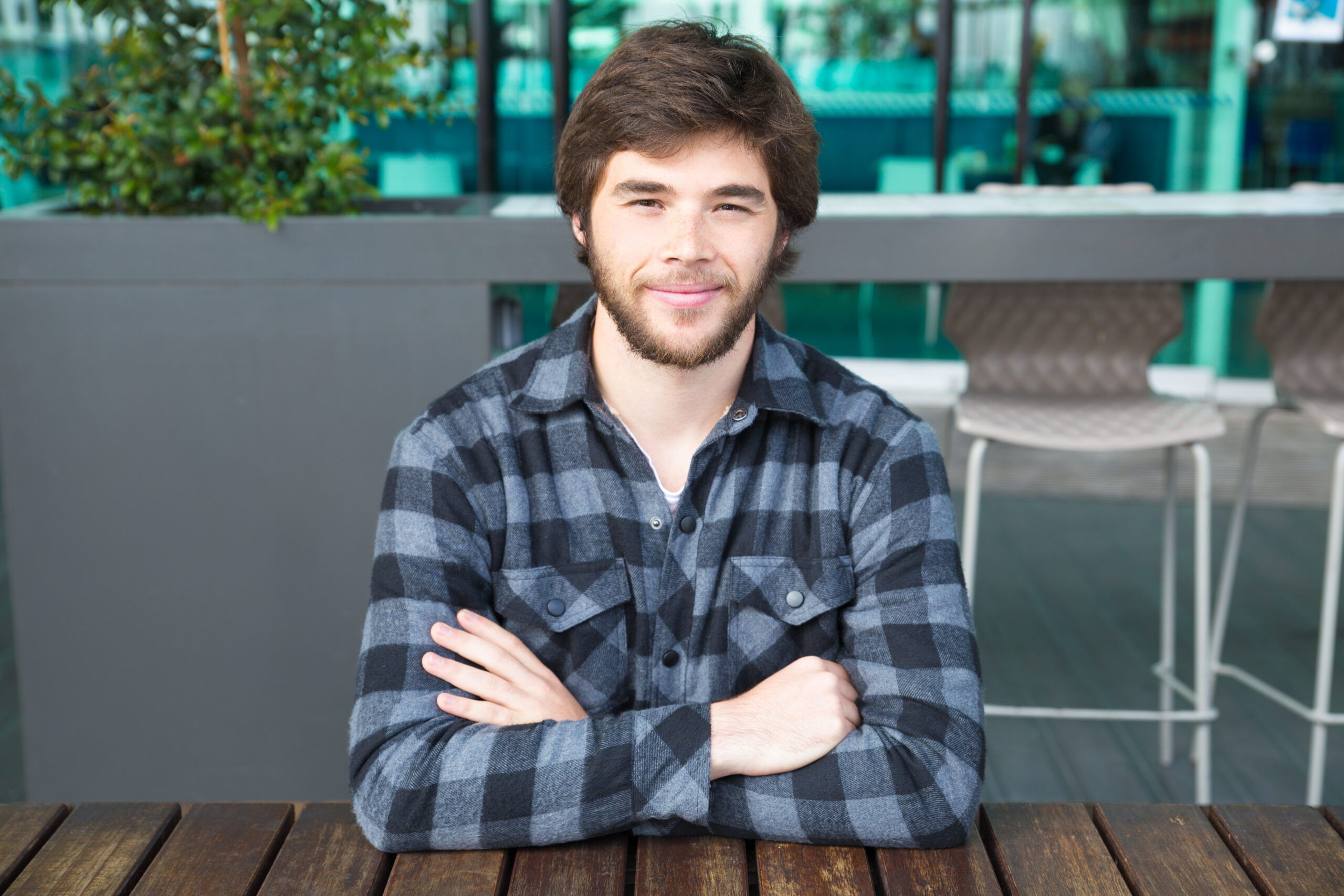 smiling man sitting at street cafe table with his arms crossed